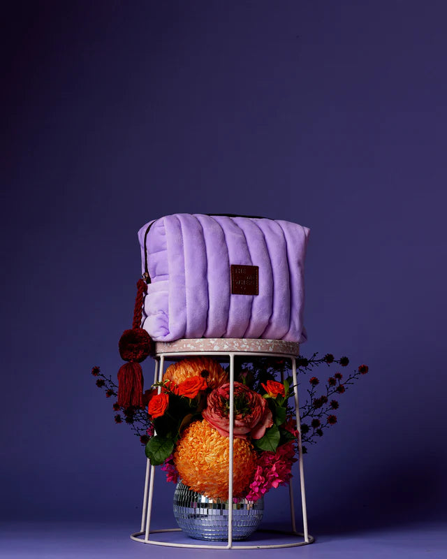 Purple quilted bag on a decorative stand with flowers against a dark purple background