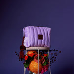 Purple quilted bag on a decorative stand with flowers against a dark purple background