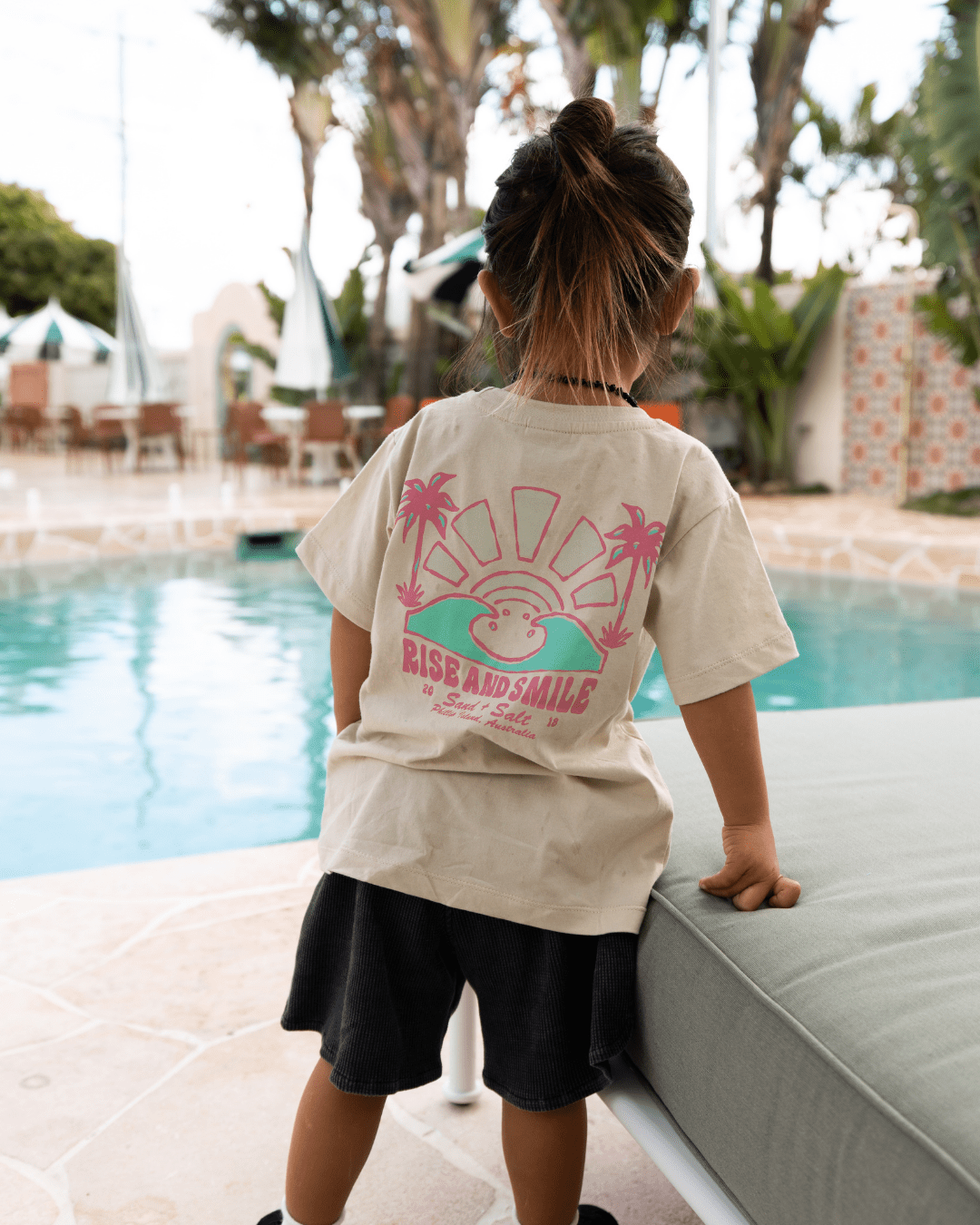 Child wearing a t-shirt with a graphic design by a poolside