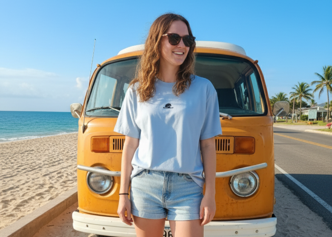 Woman standing in front of a vintage orange van on a sandy beach.