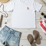 White t-shirt with a small red logo, denim shorts, brown flip-flops, and beach accessories on a wooden surface.