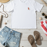 White t-shirt with a small red logo, denim shorts, brown flip-flops, and beach accessories on a wooden surface.