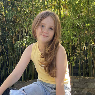 Child sitting on a panda-shaped object outdoors with bamboo plants in the background
