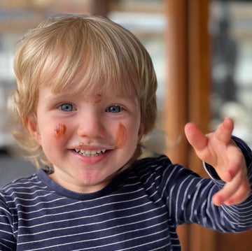 Child with paint on face and arm, wearing a striped shirt, indoors.