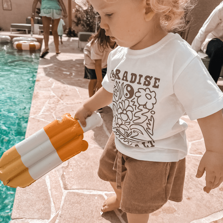 Child holding a toy by a pool with people in the background