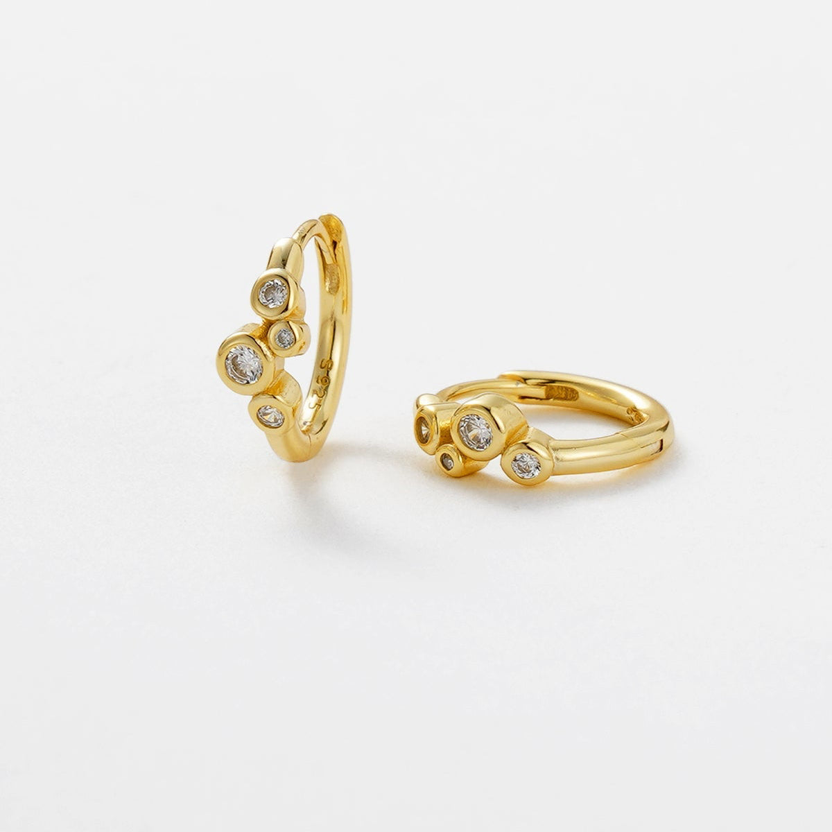 Gold hoop earring and ring with gemstones on a light gray background