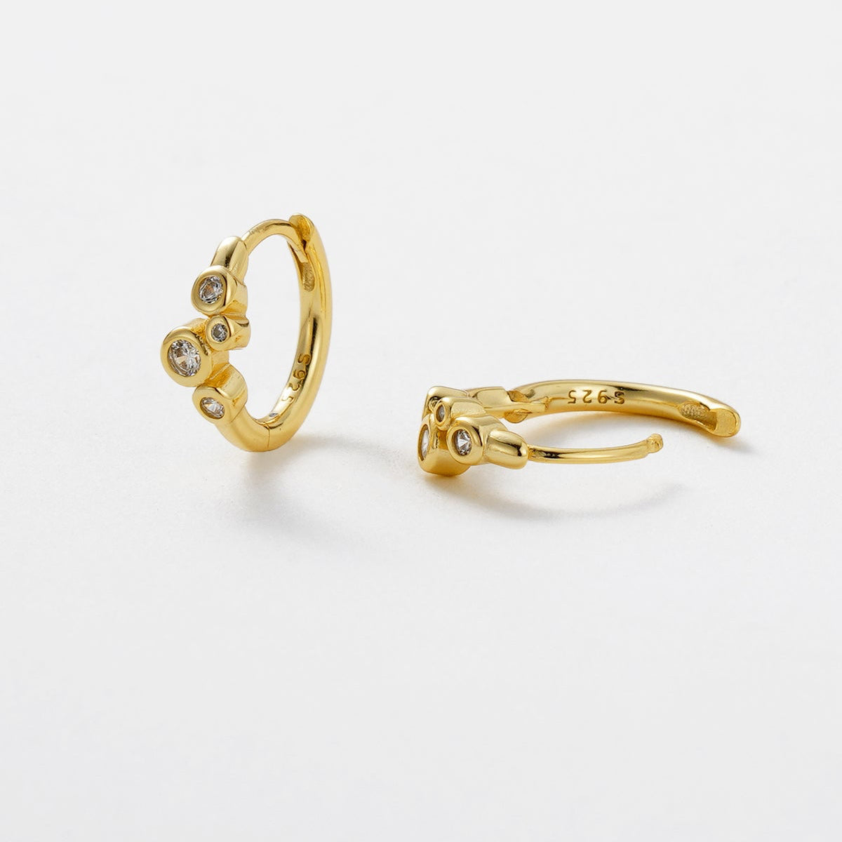 Gold hoop earrings with small stones on a light gray background