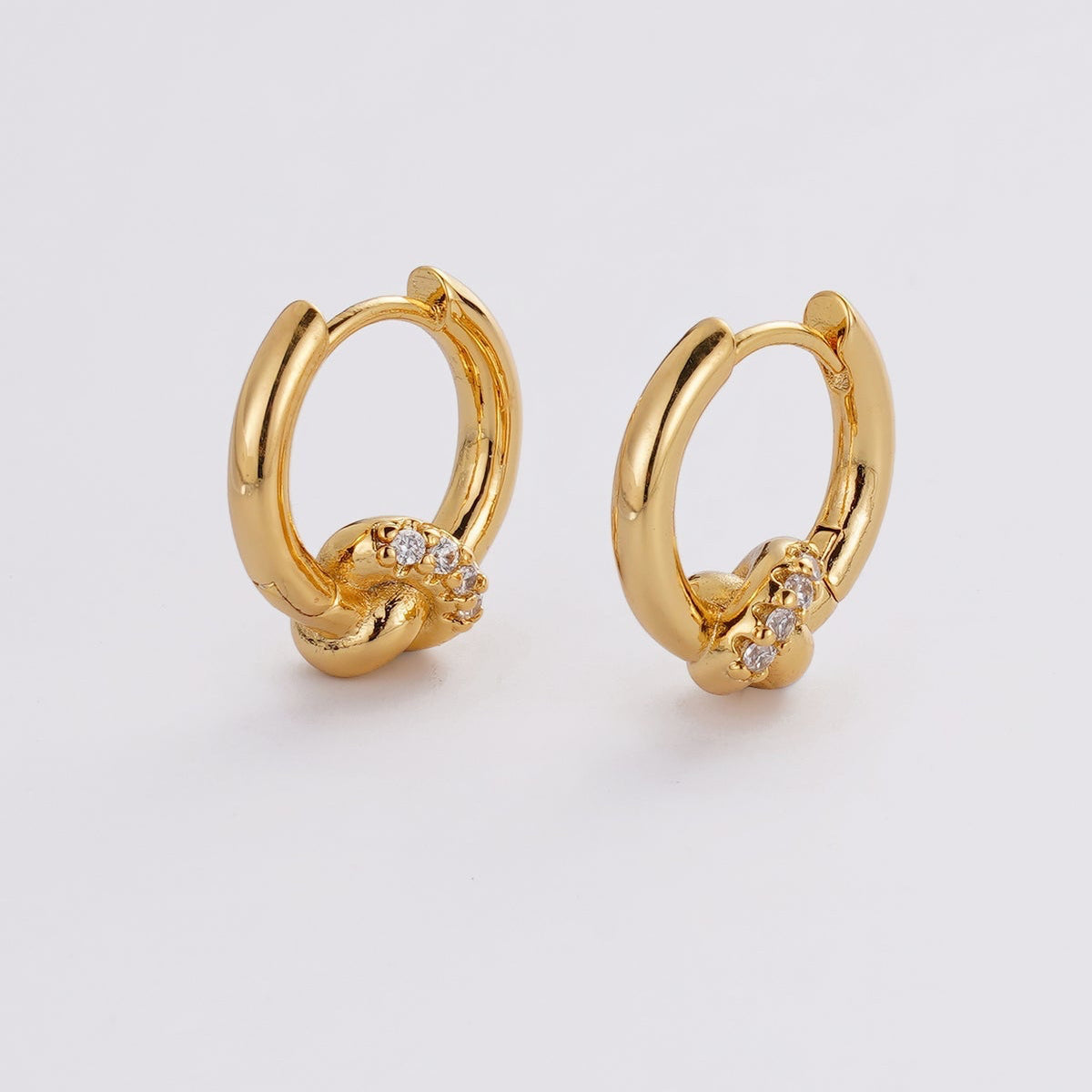 Gold hoop earrings with small diamonds on a light gray background
