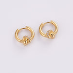 A pair of gold huggie hoop earrings with a knotted design and a small cluster of clear stones at the center, shown on a plain light gray background.