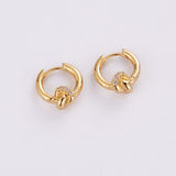A pair of gold huggie hoop earrings with a knotted design and a small cluster of clear stones at the center, shown on a plain light gray background.