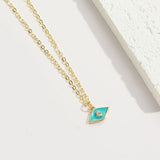 A gold chain necklace with an eye-shaped pendant featuring a turquoise enamel center and a small clear stone, displayed on a clean white surface.