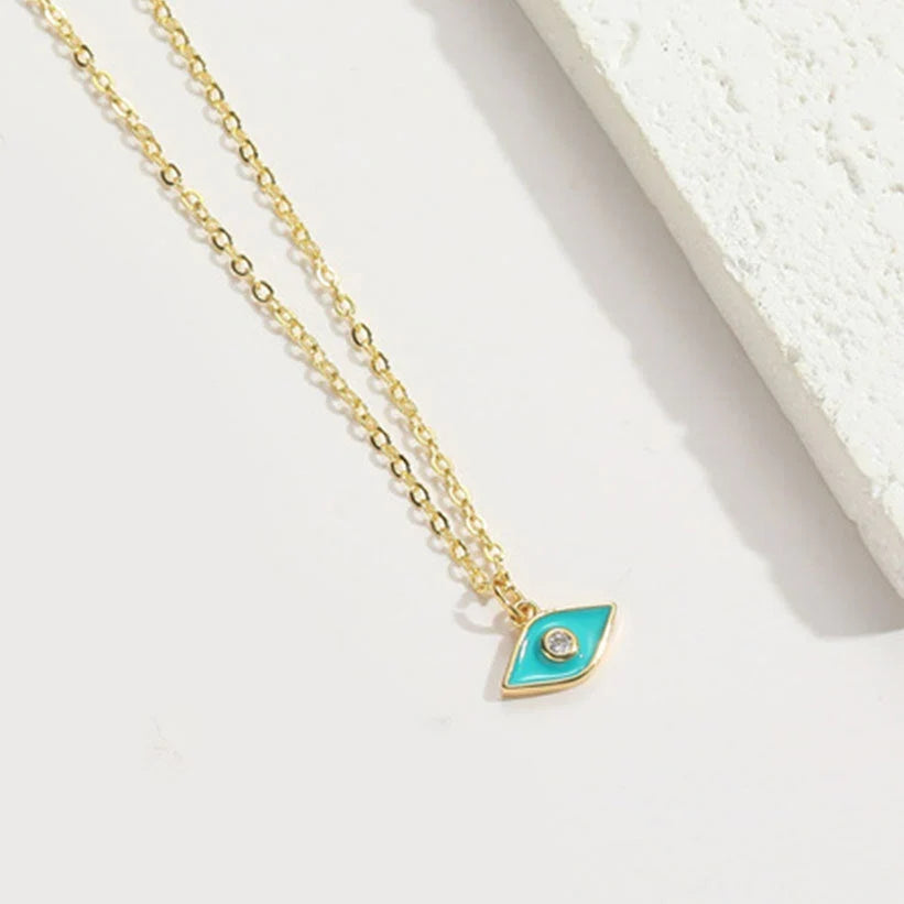 A gold chain necklace with an eye-shaped pendant featuring a turquoise enamel center and a small clear stone, displayed on a clean white surface.