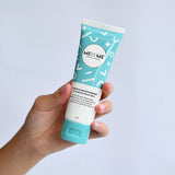 A hand holding a squeeze tube of MEBE ME Gentle Moisturiser against a light blue background.