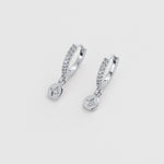 A pair of silver huggie hoop earrings with small clear stones and dangling round charms, shown on a light gray background.