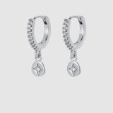 A pair of silver huggie hoop earrings with a curved row of small clear stones and a dangling round star-shaped charm, shown on a light gray background.