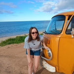 Woman leaning against a yellow van by the ocean