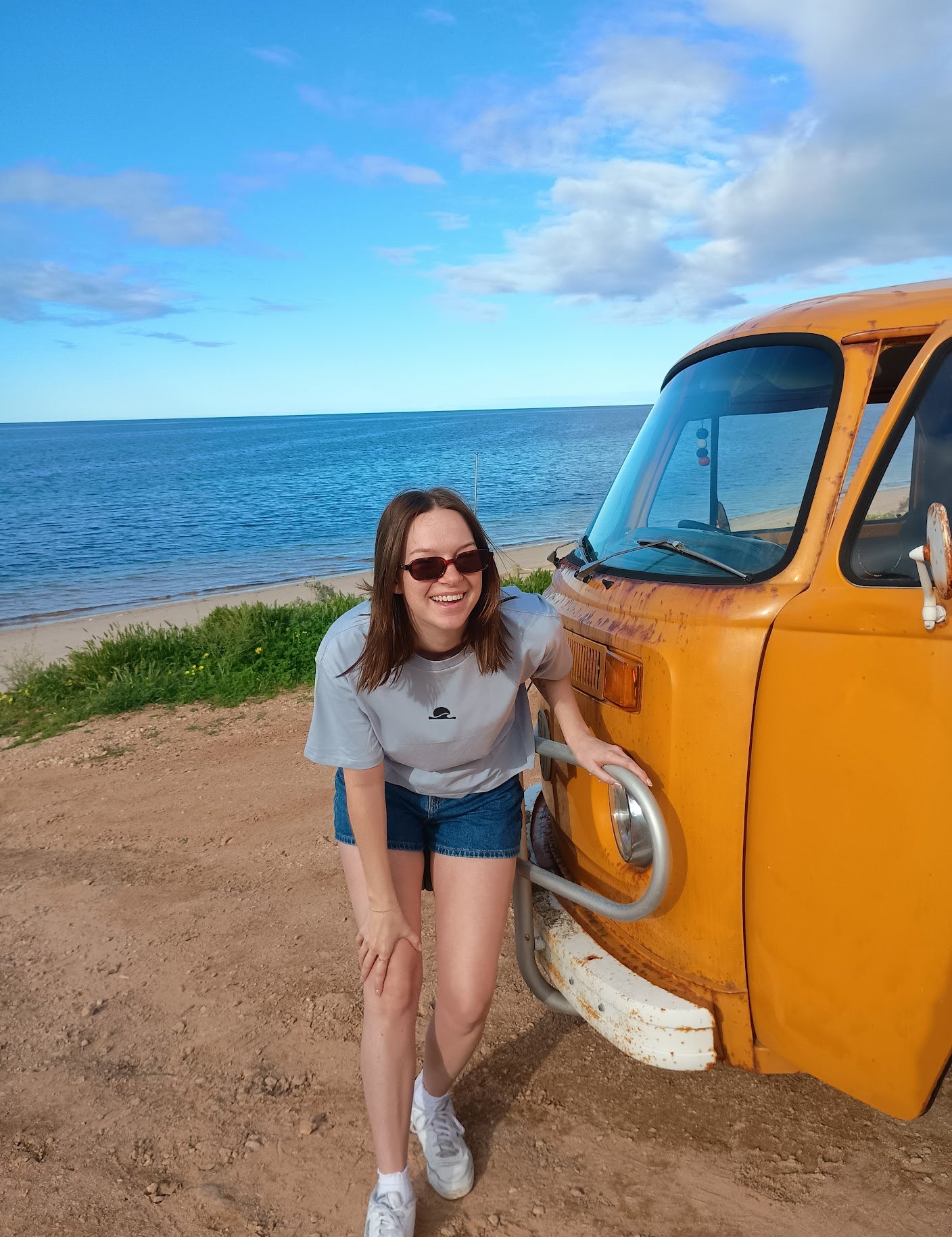 Woman leaning against a yellow van by the ocean