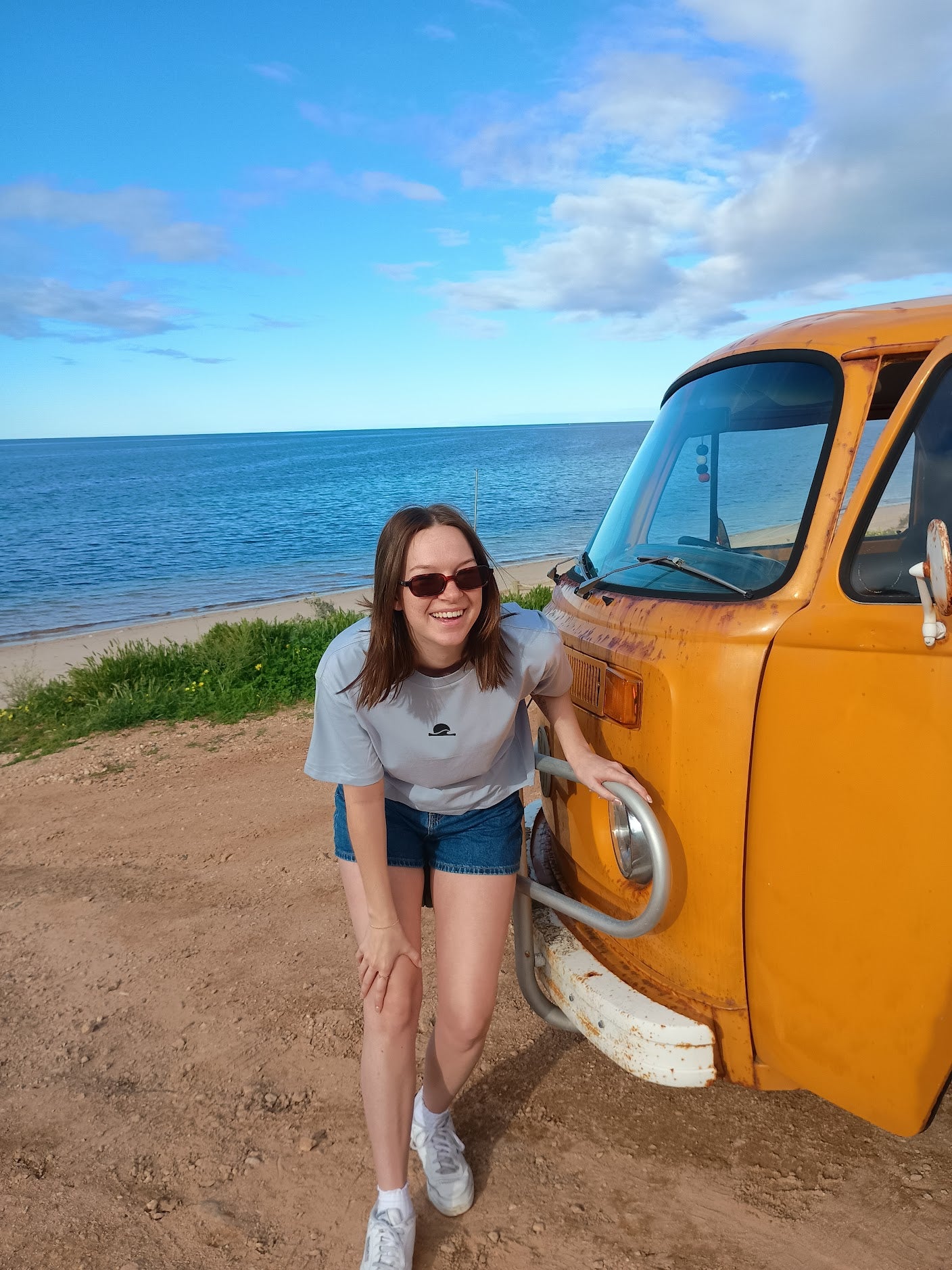 Woman leaning against a yellow van by the ocean