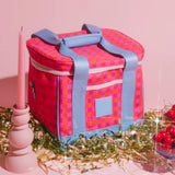 Pink and blue checkered cooler bag on a pink background with decorative elements.