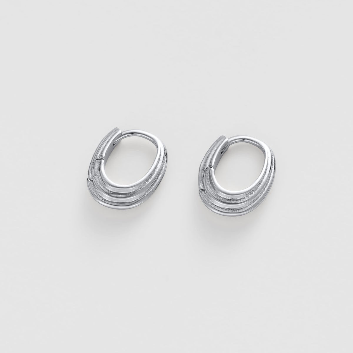 A pair of silver-toned, twisted oval hoop earrings on a light gray background.