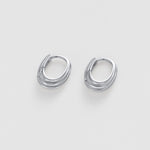 A pair of silver-toned, twisted oval hoop earrings on a light gray background.