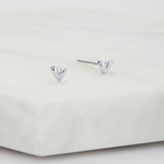 A pair of small polished silver heart stud earrings resting on a white marble block against a clean white background.