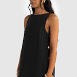 Woman wearing a black sleeveless dress with buttons on a white background