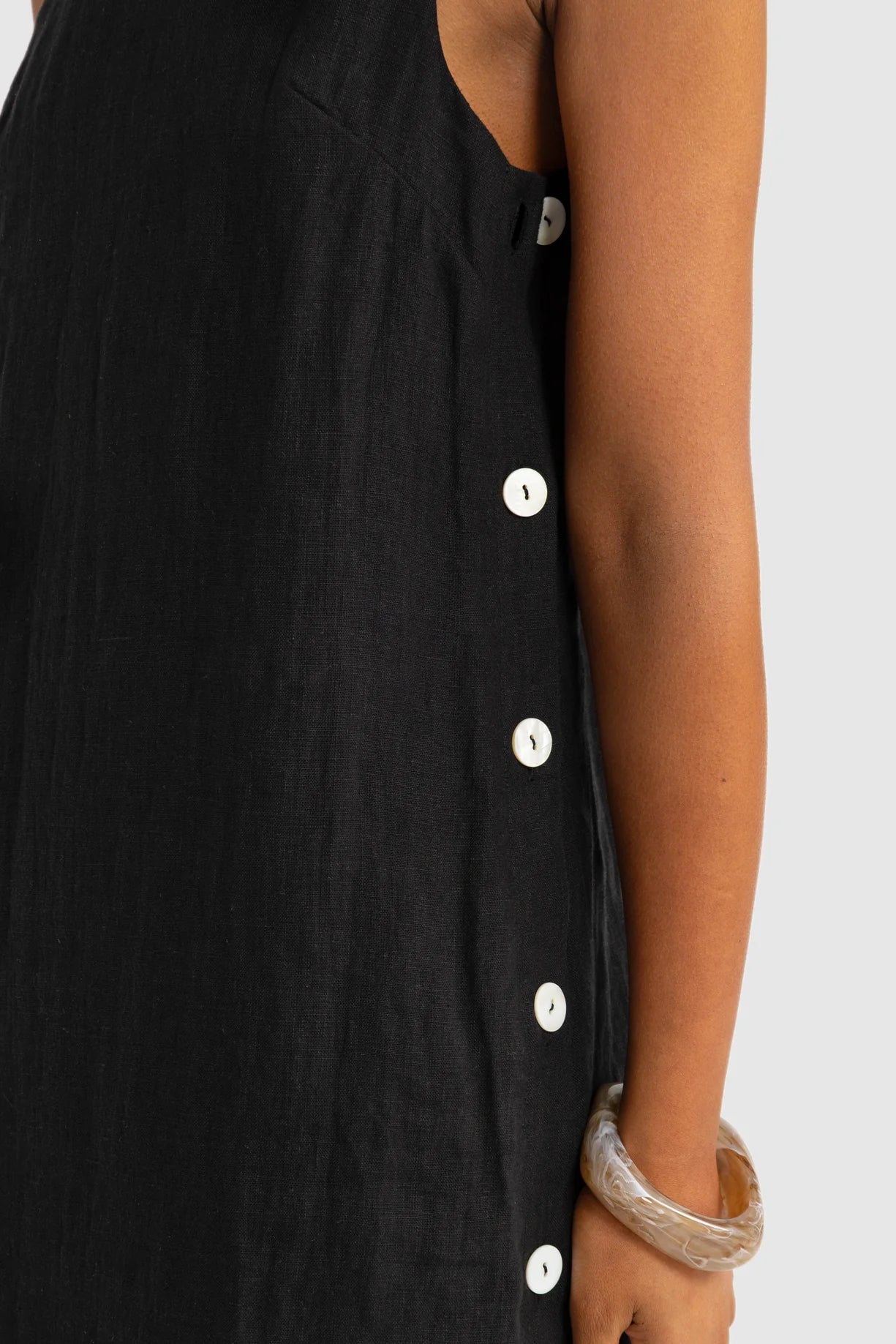 Black sleeveless dress with white buttons on a plain background