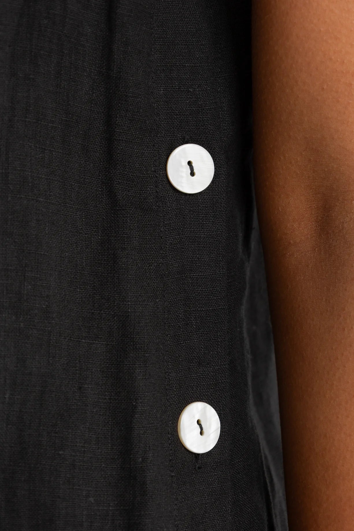Close-up of a black shirt with white buttons on a person's arm.