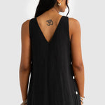 Person wearing a black sleeveless dress with white buttons on a plain background