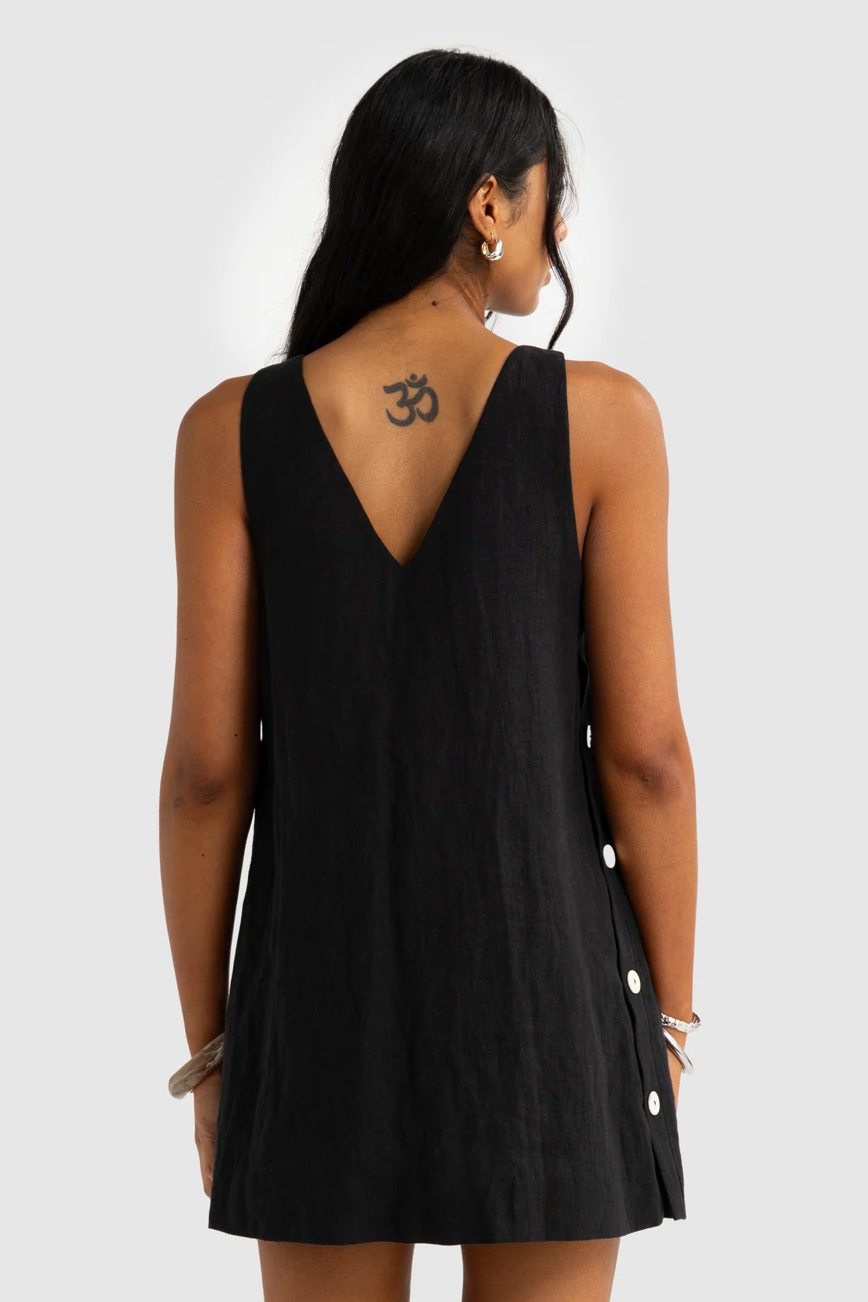 Person wearing a black sleeveless dress with white buttons on a plain background