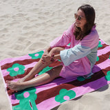 Woman sitting on a colorful towel with floral patterns on a sandy beach.
