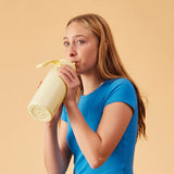 Woman drinking from a yellow water bottle against a beige background
