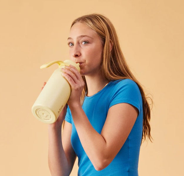 Woman drinking from a yellow water bottle against a beige background