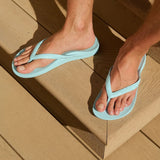 Person wearing light blue flip-flops on a wooden floor