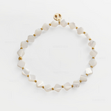 A delicate beaded bracelet made of irregular white mother-of-pearl beads separated by small gold spacer beads, with a gold clasp featuring a circular logo, displayed on a clean white background.