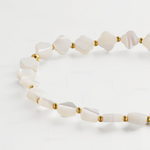 A close-up of a beaded necklace featuring irregular white mother-of-pearl shell beads separated by small gold spacer beads, arranged on a clean white background.