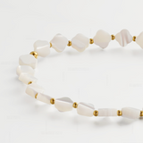 A close-up of a beaded necklace featuring irregular white mother-of-pearl shell beads separated by small gold spacer beads, arranged on a clean white background.