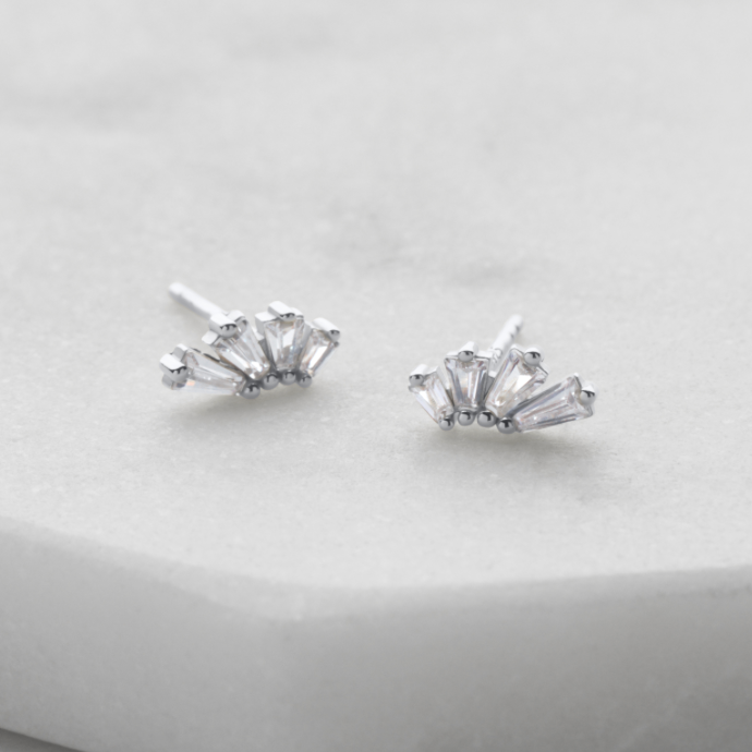 A pair of silver stud earrings with a small cluster of clear marquise-cut crystals, displayed on a light gray stone surface.